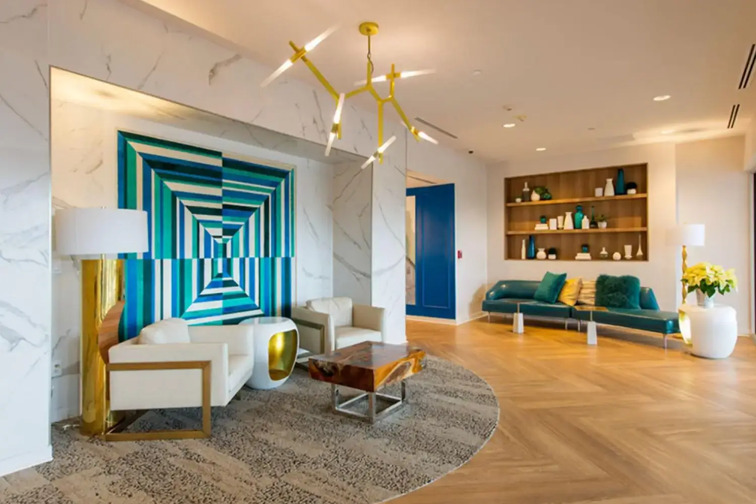 community living area with a white, blue and gold color scheme, wooden flooring, white chairs, gold coffee table, and a blue door.”