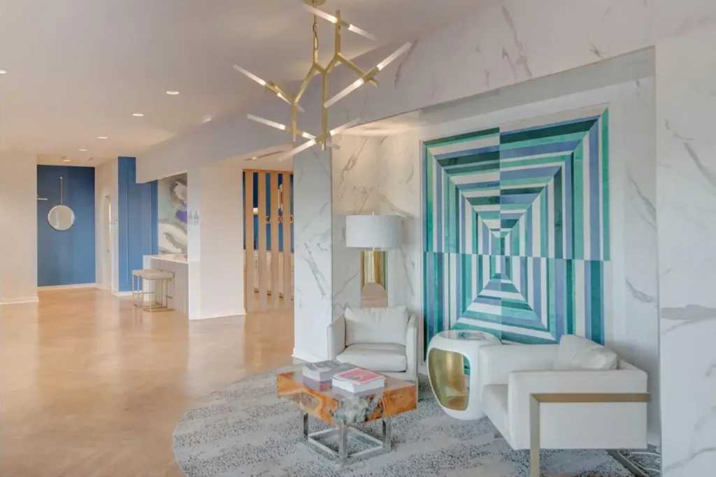 community living area with a white, blue and gold color scheme, wooden flooring, white chairs, gold coffee table, and a blue door.”