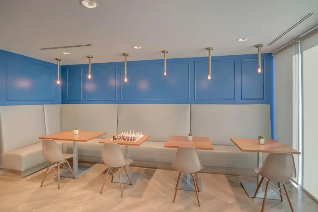 Modern, minimalist cafe interior with white walls, blue panels, wooden tables, white chairs, and a chess board.