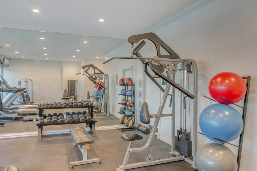 Gym with various exercise equipment including treadmills, ellipticals, stationary bike, weight rack, and a blue exercise ball.