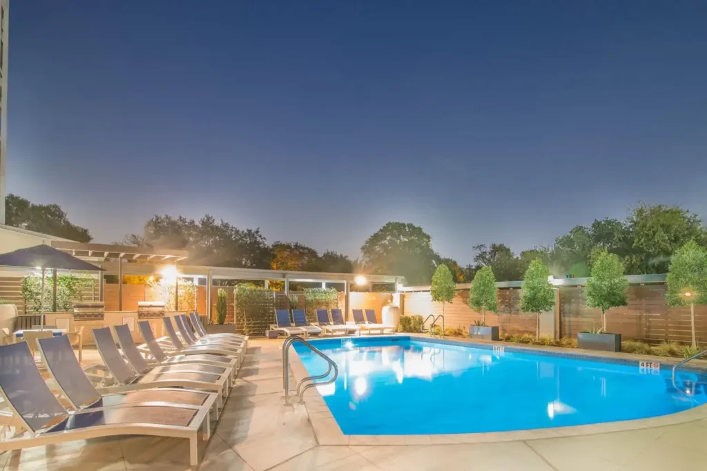 Nighttime view of the swimming pool lit with blue lights, surrounded by lounge chairs and umbrellas.