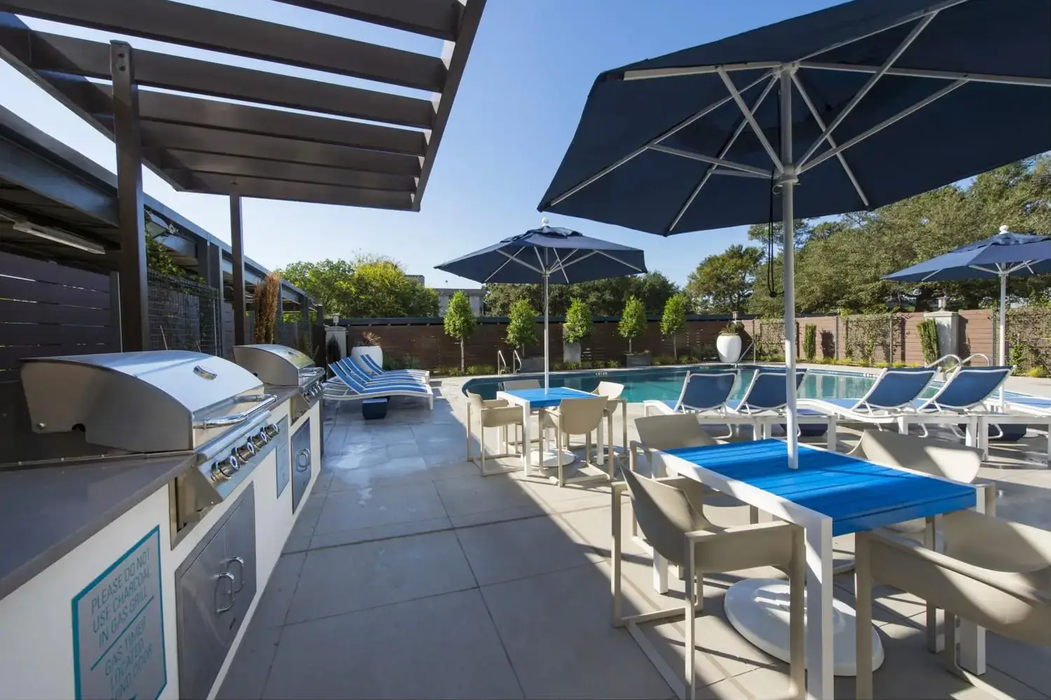 Community area with a pool, grill, blue and white polled umbrellas, lounge chairs, and a wooden pergola.