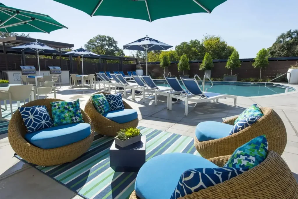 Pool area white lounge chairs with blue cushions, blue umbrellas, and wicker chairs in the foreground.