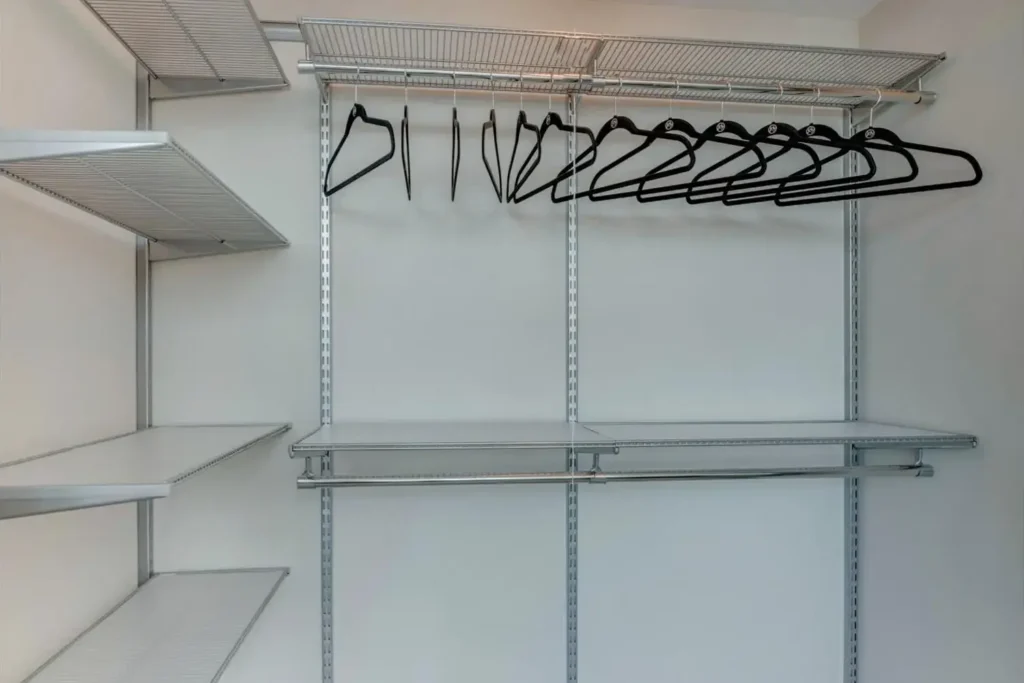Empty closet with wire shelves and black hangers, set against a white wall.