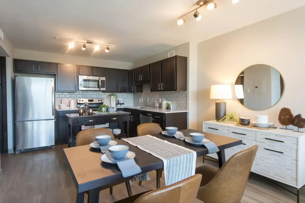 Modern kitchen with dark wood cabinets, stainless steel fridge, gas range, and a dining area with a wooden table.