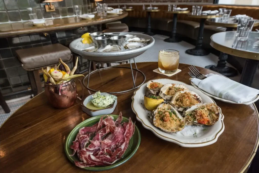 Restaurant table with a variety of dishes, including a two-tiered stand with oysters and clams, and drinks in copper mug and glass.