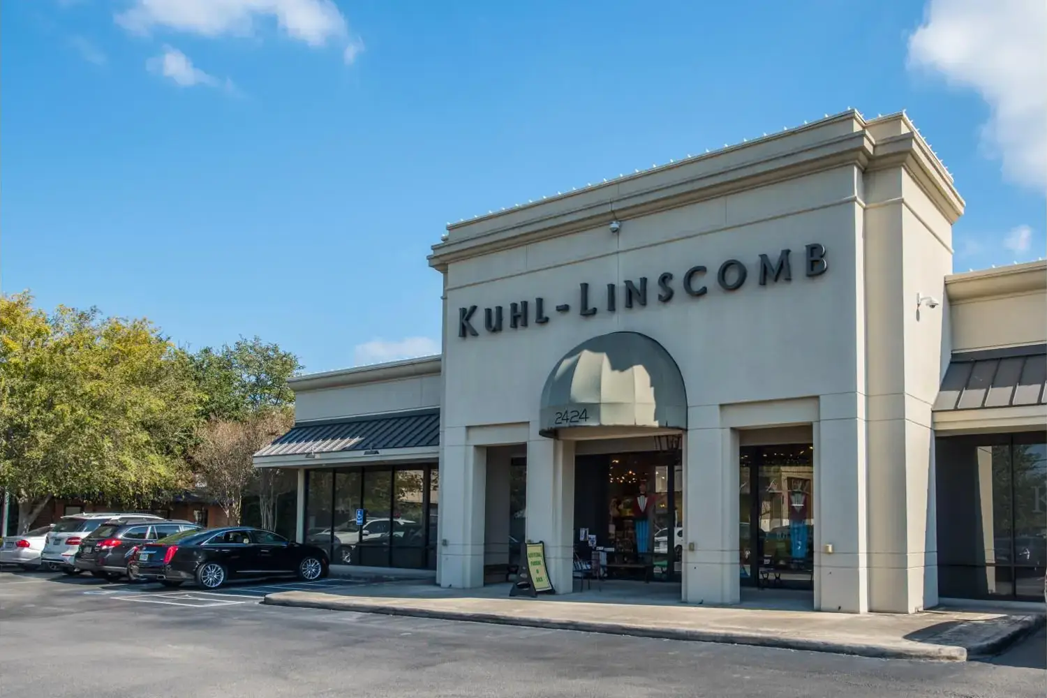 Modern storefront with a parking lot, featuring a sign reading ‘Kuhl-Linscomb’ and a large window on the right side of the entrance.